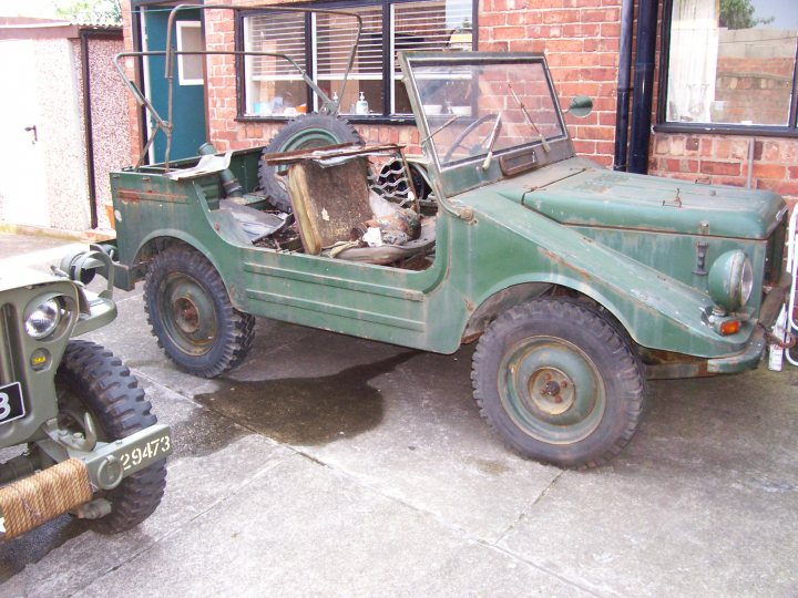 Munga Pistonheads Jeep - This image features a dilapidated, vintage military jeep parked on a cement surface. The jeep has a distinctive olive-green color and is equipped with large, sturdy tires. It's an older model, as indicated by the heavy construction and weathered appearance. The condition of the jeep suggests it might be abandoned or decommissioned, adding a sense of history and nostalgia to the scene. In the background, the remnants of a brick building can be seen, which might have some relevance to the jeep's presence in this location.