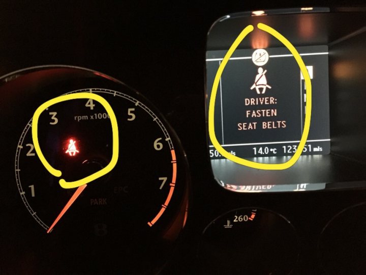 A close up of a cell phone on a table - Pistonheads - The image features a car dashboard with a potential malfunction indicator (PMI) concerning the driver's seat belts. The PMI is highlighted in two yellow circles, drawing attention to the issue. The temperature gauge is also visible, showing it's at 140 degrees Celsius. The view provides a lit candle, which is unrelated to the car's warning lights, and the photograph has a holiday-themed "round Christmas tree" doodle on it.