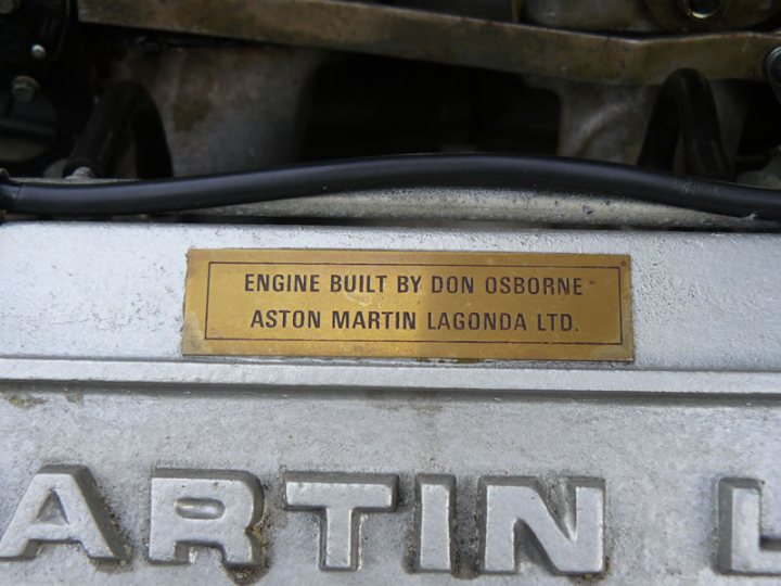 So who did your 'Final Inspection'? - Page 10 - Aston Martin - PistonHeads - The image presents an interesting juxtaposition of text and location. Dominating the scene is a large metal plate bearing the words "ENGINE BUILT BY DON OSBORNE" and "ASTON MARTIN LAGONDA LTD". This plate suggests that this machinery belongs to a company renowned for its high-quality automobiles.

Despite the text's prominence, the plate itself is slightly worn and soiled, indicating some level of use. The plate is affixed to a metal bar or rod, which runs horizontally across the image, serving as a stark contrast to the ornate text.

The setting for this plate is not immediately clear from the image, but the observant viewer might deduce that it is situated outdoors. An intriguing detail that catches the eye is the presence of a spider on the plate, adding a touch of organic life to an otherwise mechanical scene.