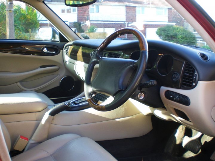 Jaguar Pistonheads Xjr - The image showcases the interior of a car, viewed from the perspective of the driver. The steering wheel is prominently featured, indicating the right side driver's view. The dashboard is visible, with the instrument panel and center console in focus, displaying a well-equipped cabin. The car has leather upholstery, as evidenced by the textured appearance of the seats. The car is parked near houses, suggesting a residential area.