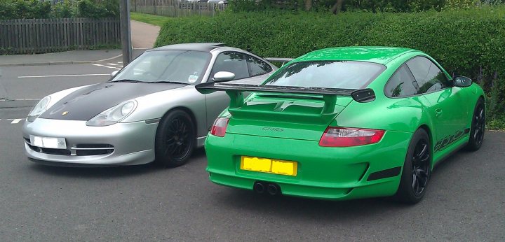 Show off your GT, past and present... - Page 12 - 911/Carrera GT - PistonHeads - The image captures a parking lot where two luxury sports cars are parked. On the left, there's a silver Porsche, characterized by its sleek design and iconic symbol on the hood. On the right, a vibrant green Porsche stands out with its rear-wing spoiler, adding to its sporty aesthetic. The cars, with their distinctive accents and precise bodywork, dominate the scene, indicating a common interest in high-performance vehicles.