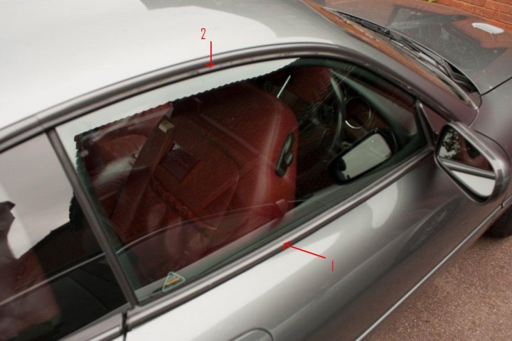 Trims Side Pistonheads Window - The image shows the interior of a car's driver's seat through the open window. The viewer is looking from outside the vehicle at the side window, which is adjacent to the passenger's seat. The inside of the car appears organized and maintained, with a focus on the back of the driver's seat, which is mauve in color. The driver's side mirror can be seen from this perspective, reflecting the car's bodywork. There are red lines across the photo, possibly indicating measurements or points of interest. The photograph has a candid, documentary feel.