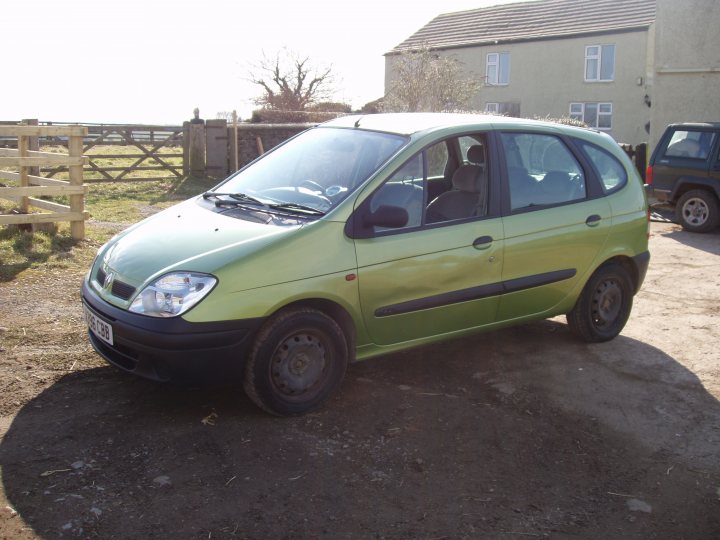 my first car  - Page 1 - Readers' Cars - PistonHeads - The image shows a green hatchback car parked on a compacted gravel driveway. The car is a hatchback model and has a visible dent on the left side of its hood, indicating it may have been in a collision. The vehicle is positioned near a fence to the left and is in front of a house with windows and a garage. The sky is clear, suggesting a sunny day, and there is grass on the ground, indicating that this could be a rural or suburban area.