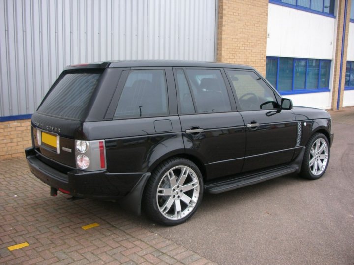 Pistonheads Rover Range Sell - The image showcases a black Range Rover Evoque car parked in front of a building. It features a robust and modern design, with a sleek body that appears polished, suggesting well-maintained or possibly a new or newly serviced vehicle. The car is equipped with large and glossy black rims, and it is resting on a gravelly parking lot. The background consists of a brick wall, green grass, and a wooden fence, indicating a landscaped yard or parking area adjacent to the building. The car's prominent features and the detailed background create a harmonious scene of automotive elegance and urban tranquility.