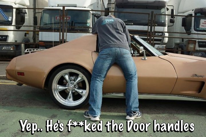 Caption Competition. What exactly is Vaughan doing ? - Page 1 - Corvettes - PistonHeads - The image depicts a person standing behind an old, tan-colored sports car. The individual is leaning forward, appearing to look inside the vehicle, while the car is parked with a narrow space between jack-knife trucks behind it. The photo includes a text overlay that reads, "Yep. He's f***ked the Door handles." The image presents a humorous comment on the state of the car's door handles, implying damage or misuse of the car.