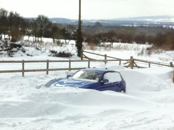 Pics of your car in the SNOW - Page 46 - General Gassing - PistonHeads - In a blend of nature and human-made structures, a scene unfolds where winter's touch is evident. A car, dusted with recent snowfall, is parked amidst the pristine whiteness. The vehicle's doors are hidden under the high snowbank it sits in, while piles of snow rise up against it, partially covering the car. A fence, possibly marking a boundary, stands in the foreground, adding a sense of depth and structure to the image. Further back, the landscape features trees standing tall against the snowy backdrop, their branches blanketed in snow. The overall image conveys a peaceful winter scene, presenting a snapshot of life where winter's impact is unmistakable.