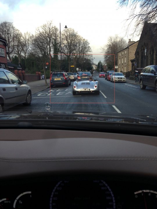 A car driving down a street next to a traffic light - Pistonheads - The image shows a perspective from the driver's seat inside a car, capturing a view of the road ahead. An outdated model, possibly an Audi, is seen driving on the street, with a tree-lined sidewalk and desolate urban surroundings. Other cars are visible on the street as well, suggesting a calm, suburban area. The color palette is dominated by muted tones, with the faded colors further emphasizing the dated quality of the car's interior.