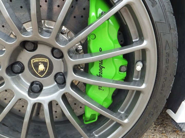 Challenge Stradale - brake calipers colour - Page 1 - Ferrari V8 - PistonHeads - The image captures a close-up view of the rear wheel of a Lamborghini. The wheel is adorned with a green object, possibly a wheel stop or a paint gun. This vibrant color pops against the silver metal and black tire. The spokes of the alloy wheel are sharply angled, creating a dynamic and elegant pattern. The fender and tire can be seen in the background, but the green object is the focal point of the image.