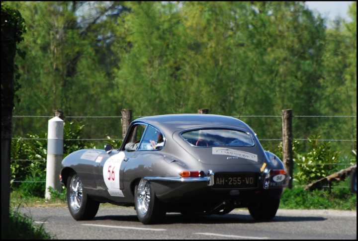 The Tour Auto came to town - Page 1 - Classic Cars and Yesterday's Heroes - PistonHeads - The image depicts an old-fashioned car driving on a paved road. The car appears to be vintage, as indicated by the distinctive shape and design elements. The background of the image indicates a rural or semi-rural area with trees lining both sides of the road. There is a watermark or emblem on the side of the car, however, the specific content or context of the image is not clear due to resolution limitations. The photo seems to have been taken during the daytime under clear weather conditions.