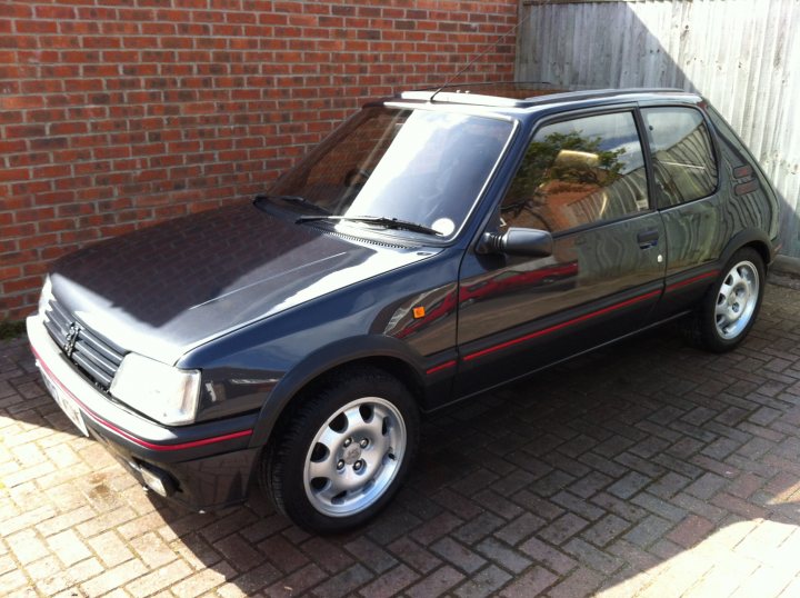 A car parked in a parking lot next to a car - Pistonheads - The image features a sleek, black two-door coupe parked on a brick driveway. The vehicle's shiny body reflects the surroundings, the sunlight enhancing its reflective surface. The car is positioned slightly diagonally to the driveway, giving the image a dynamic feel. Its red and white detailing at the bottom gives a stylish contrast to the black body. In the distance, an old brick wall adds a touch of vintage charm to the scene.