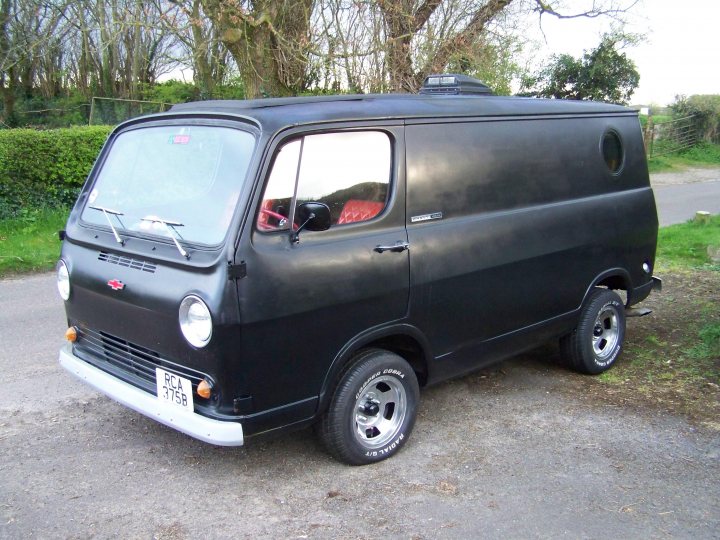 Tough and reliable classic for "everyday" use? - Page 3 - Classic Cars and Yesterday's Heroes - PistonHeads UK - The image shows an old black van parked on a gravel surface. It is equipped with a black spare tire mounted on the roof, which gives it a distinctive look. The van has visible windows and a door, suggesting it could be used for both cargo and passengers. There are no texts or other distinguishing marks visible in the image. The vehicle appears to be in a rural setting due to the gravel surface and lack of modern buildings in the immediate background.