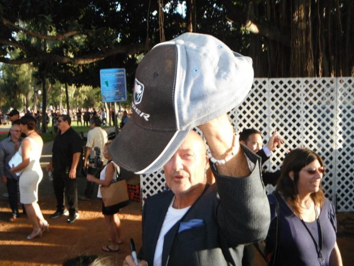 Pistonheads - The image captures a lively outdoor scene where a group of people are gathered. In the foreground, a man is holding a baseball cap, which has a sports team logo, likely displaying it proudly. He is dressed smartly in a jacket and tie, suggesting a formal event or occasion. A number of other individuals, both in the background and in the periphery, are engaged in conversation and socializing. The setting appears to be a public area or park, as indicated by the presence of trees and casual attire among the crowd.