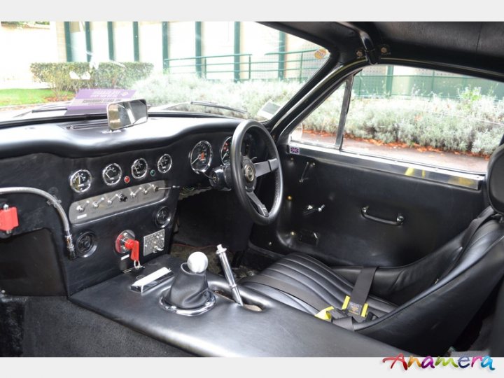 Early TVR Pictures - Page 36 - Classics - PistonHeads - The image is a photograph focused on the interior of a car, specifically capturing the side view from the driver's seat towards the front of the vehicle. The car's interior is primarily black, with the upholstery and interior surfaces being predominantly dark in color. The dashboard features a variety of gauges and controls, typical of older car models, and there are various switches and a stereo system visible among these controls.