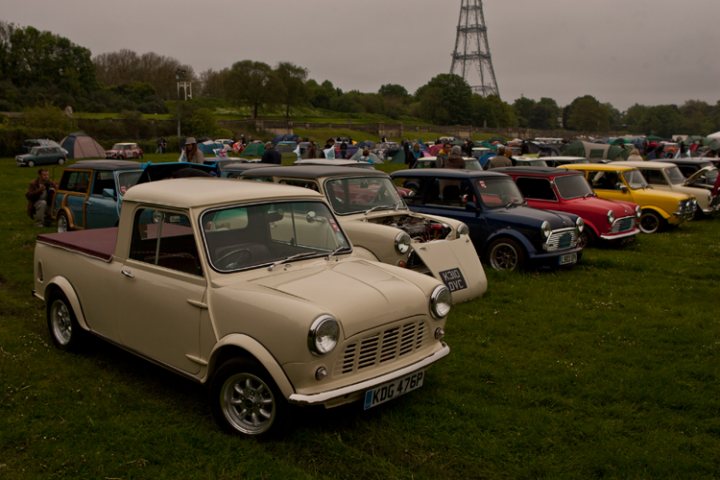 London to Brighton  - Page 1 - Classic Minis - PistonHeads - The image portrays an event celebrating vintage vehicles, specifically an antique car show, on a grassy field. A variety of classic vehicles, including several antique cars, are parked in a line, their hoods likely to be open to share their engines with visitors. Among them, their colors range from vintage hues like beige and pristine whites to more vibrant colors like red and blue, suggesting a wide spectrum of vehicle history represented. The spectators, present in the background, appear to be enjoying the exhibition, contributing to an atmosphere of community and shared passion for automotive history. The towering pylon in the distance adds a unique backdrop to the event.