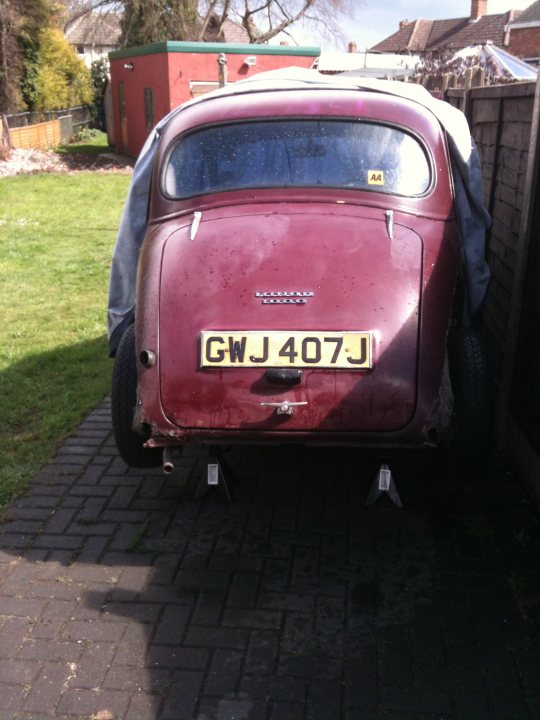 1971 Morris Minor 1000 Resto thread (Maybe) - Page 1 - Classic Cars and Yesterday's Heroes - PistonHeads - The image shows a vintage car parked in a driveway. The car appears to be of an older model, with a red body that has seen some wear and tear. Its license plate is clearly visible and reads "GWJ 407J." The driveway is paved with dark bricks, and the car is positioned in a way that suggests it's parked to the side of the driveway. The backdrop consists of a grassy area and a fence. The sky above is overcast, suggesting it might be a cool or cloudy day.