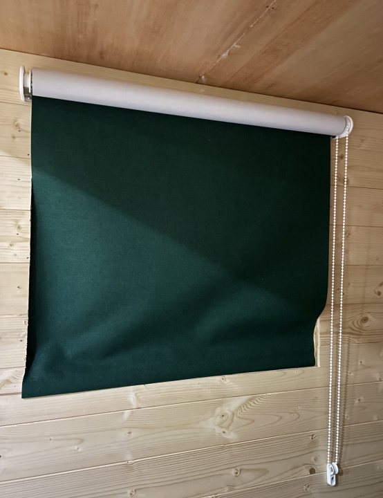 The canal / narrowboat thread. - Page 36 - Boats, Planes & Trains - PistonHeads UK - The image displays a dark green window curtain with vertical slats. It is partially closed, revealing only the upper portion. The curtain has a textured fabric and appears to be made of felt material. Behind the curtain, there's a white surface, possibly a wall or panel, which contrasts with the curtain's dark color. In the bottom right corner, the edge of a wooden floor can be seen, indicating that this scene is set in an indoor room or cabin. The style of the image is straightforward and appears to serve a functional purpose, perhaps for showcasing the curtain's design or as part of a product catalog.