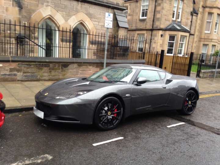 A car parked on the side of the road - Pistonheads - The image depicts a city street scene. A prominent feature in the median is a sleek, modern sports car. The car appears to be moving on the road, as suggested by its registration plate. The registration indicates it is registered in the UK, as evidenced by the British-style license plate. The sports car is parked on the right side of the road, which differs from the driver's side, due to regulations in left-hand-drive countries. The background of the image shows a street with sidewalks and buildings, indicating a residential area.