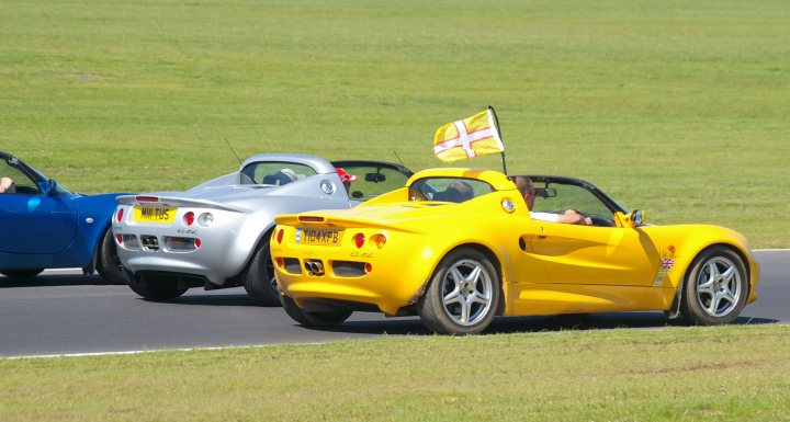 Snetterton Lotus Festival 25/26 June - Page 1 - General Lotus Stuff - PistonHeads - The image showcases a sunny day on a race track, with three sports cars in action. One of the notable features is a sports car prominently displaying a British flag on it, indicating its possible use in a competition. The cars are moving on the track, showcasing individual racing styles. The third car seems to be from a rough track racing event. The scene evokes a sense of speed and competition, with the vibrant colors of the cars standing out against the green of the grassy track and the clear blue sky.