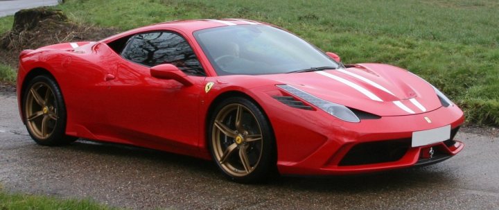 A red and white car with a red bow on it - Pistonheads - The image depicts a vibrant red sports car, specifically a Ferrari, parked on a road with lush green grass surrounding the area. The vehicle's sleek design features classic Ferrari styling with a low-lying body and slender headlights. The sports car's front wheels are angled towards the camera, revealing its eye-catching alloy rims. The car's door window is also clearly visible, reflecting a tranquil setting away from the urban hustle and bustle.