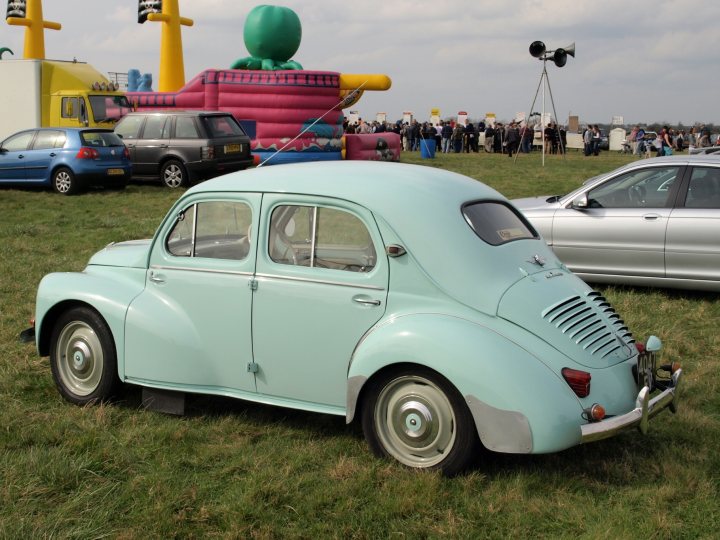 Anyone know what this car is? - Page 1 - French Bred - PistonHeads - In the image, an expansive grassy field is filled with a variety of vehicles. A mint green classic car, with chrome bumpers and other details, is the focal point of the image, parked on the grass. The field is bordered by various vehicles, including a blue station wagon, a yellow truck, and a pink and purple inflatable play area added a playful touch to the scene. A few people can be seen scattered around the field, adding life to the vehicle-filled landscape. Above is a gray, cloudy sky, suggesting a possible event or gathering in the vicinity.