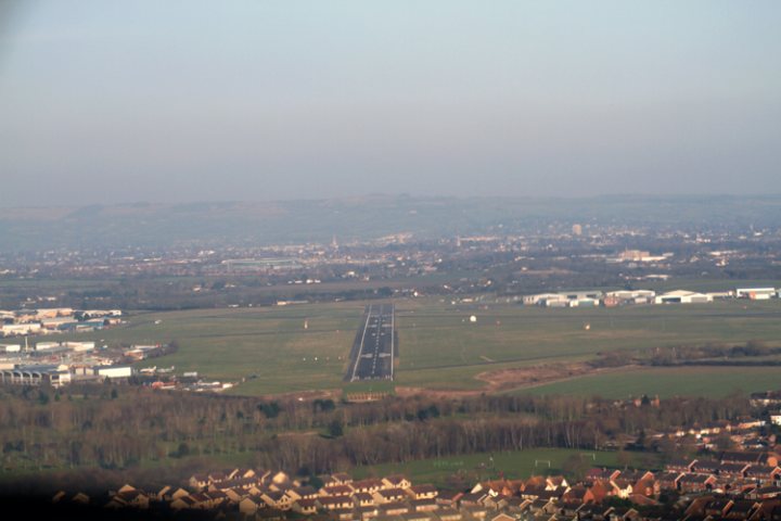 Fancied some fish for lunch - Page 1 - Food, Drink & Restaurants - PistonHeads - The image captures a bird's eye view of a sprawling town nestled near a runway. The runway, a straight path, is surrounded on three sides by the residential and industrial areas, creating a distinct boundary between the two. The color palette of the image is predominantly neutral, with the strips of green from the tree-lined streets and the expansive field contrasting against the blue sky. The runway's proximity to the town suggests a significant link to air transportation for this community. The overall composition of the image exemplifies urban planning, juxtaposing residential and industrial zones with transportation infrastructure.