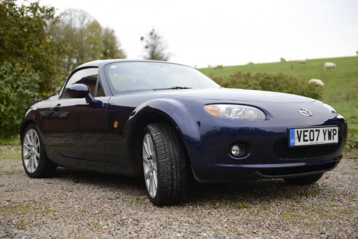 MK3 MX-5 for a 20 year old? - Page 1 - Mazda MX5/Eunos/Miata - PistonHeads - Photograph of a dark blue sports car parked on a gravel surface with grass and animal silhouettes in the background. It's a clear day with slight motion blur suggesting the photo may have been taken with a long exposure or panning technique. The vehicle features alloy wheels and the Pirelli logo is visible.