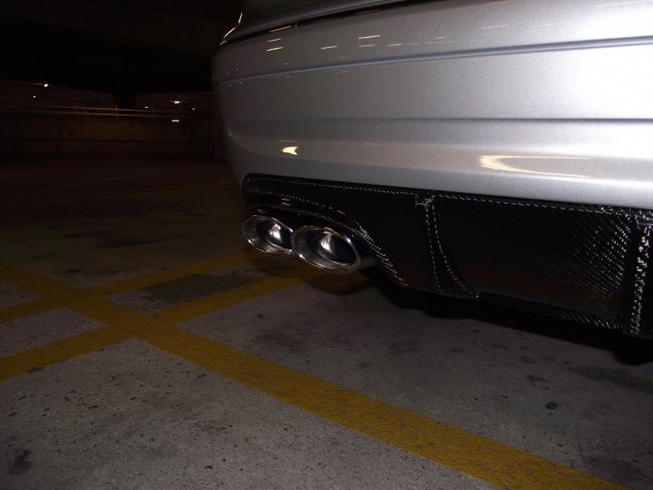 Mercedes Pistonheads - The image showcases the rear end of a vehicle, likely parked in a parking lot. The vehicle is fitted with a black bumper that has a fancy carbon fiber flavor. Attached to it are two silver rectangular exhaust pipes. The parking lot appears to be quite empty, as there are no other vehicles visible in the frame. The overall lighting of the scene suggests it might be night time.