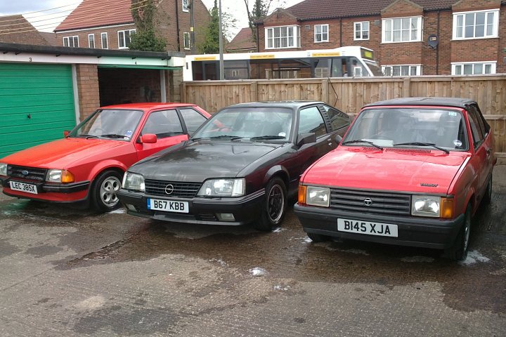 Anyone remember the Talbot Samba S? - Page 5 - Classic Cars and Yesterday's Heroes - PistonHeads - The image shows a trio of older model cars parked on a driveway. From left to right, there's a red two-door vehicle, a black car that seems to be a hatchback, and a red car, possibly a compact SUV. The cars appear to be parked in front of a garage with a green door, emphasizing the background is blurred out. The setting seems quiet and contained, with only a few cars and buildings visible. The relative positions of the cars indicate that they are parked in a line, not directly side by side.