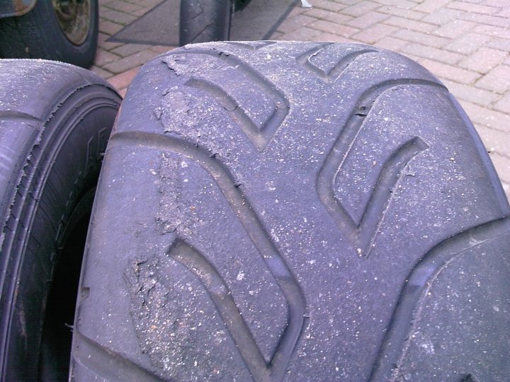 Pistonheads Suspention Reveal - The image shows the tread pattern of a tire, viewed from one side, seemingly indicating wear. There are multiple rows of tread, exhibiting patterns and grooves designed for traction. The tire is dirty, suggesting it may have been used or stored outdoors. The side wall of the tire is not visible in this angle, and the image is somewhat blurry, making some details difficult to discern. It appears to be a standard car tire.