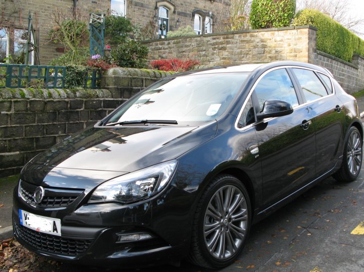 Pistonheads - This is a daytime photo of a black car parked on the left side of a street. The vehicle appears to be a hatchback or station wagon, judging by its body style. It has tinted windows, multi-spoke alloy wheels, and a prominent front grille with a small emblem in the center, which is likely the manufacturer's logo. On the windshield, there's a small sticker. The car is positioned in front of a brick wall and a house, indicating that this might be a residential area. The surrounding landscape suggests it's either spring or summer.