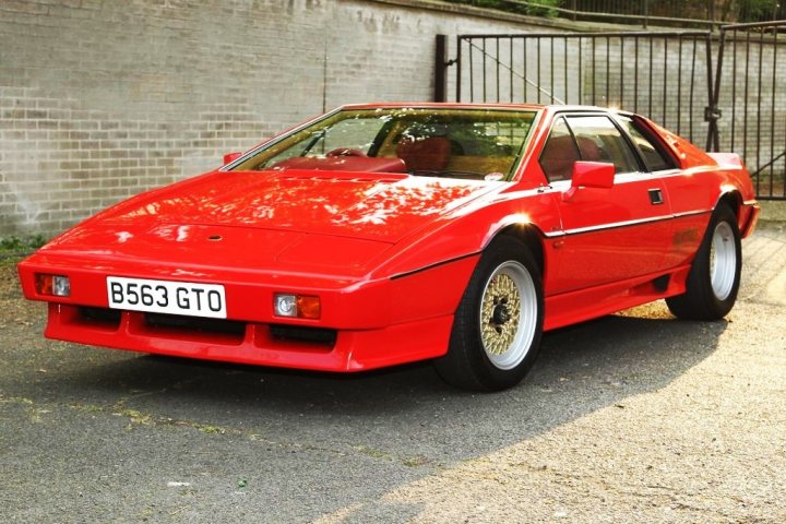 Late Pick Pistonheads - The image features a vibrant red sports car parked against a brick wall. The car appears to be a converted Pininfarina Azzurra, given its design elements and trapezoidal shape. It has a distinctive white stripe running down the center of the hood and a registration plate with the license "B563 GTO". The car is positioned sideways to the viewer, with its rear wheel being nearest to the camera.