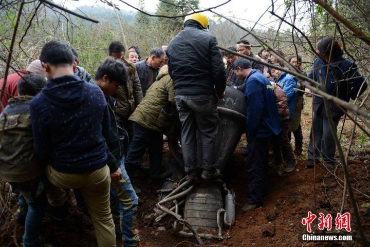 A group of people standing next to each other - Pistonheads - The image shows a group of people gathered around a scene in a wooded area with a large, dirty object in the middle. Several individuals are crouching or leaning over the object, while others are standing, looking on. The people are dressed in various styles of clothing, suggesting a diverse group. Some people are wearing winter coats, indicating the photo might have been taken in a cold environment. There are no visible texts in the image. The atmosphere suggests a shared interest or concern among the group.