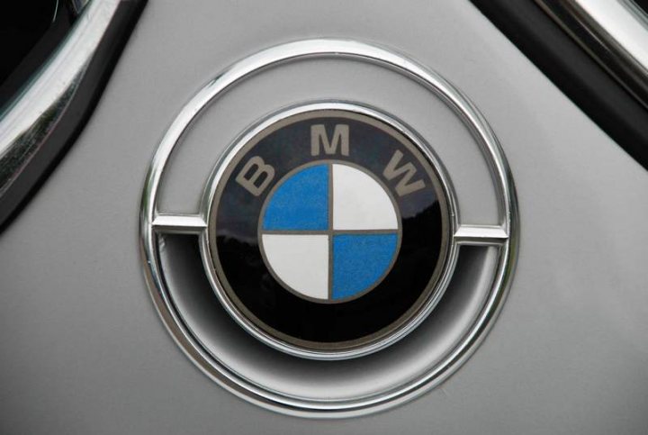 Sunday Pistonheads Service - The image features a close-up of a metallic object with a circular shape and a distinctive logo in its center. The logo consists of the letters "BMW" in black, with the letters finely detailed, surrounded by a border that is blue on the top half and white on the bottom half. The background is indistinct but appears to be a matte surface, possibly car paint in a shade of silver or gray. The style of the image is realistic and possibly intended for promotional or commercial use to emphasize the logo and the quality of the object.