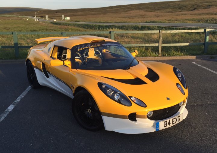 Exige S1 or S2 (Sprint / Cup) - Page 1 - Elise/Exige/Europa/340R - PistonHeads - The image captures a journey on the road, with a vibrant yellow and black Porsche Cayman sports car as the central focus. The car is parked in a lot, with its nose facing towards the right side of the frame, its sporty design accentuated by a large rear wing. The Porsche's license plate reads "B4 EXG", and it's positioned on the left side of the image. The background provides context, showing a clear sky, suggesting good weather for the car's owner or passengers. Overall, the image conveys a sense of adventure and the thrill of open roads.