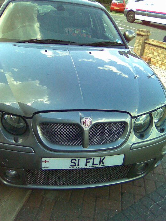 Cdti Pistonheads - The image shows a modern, silver-colored replacement car parked on a driveway. The car is a two-door coupe with a sleek design that suggests speed and efficiency. The front of the car is clearly visible, featuring the vehicle's badge and a custom plate reading "SI FLK." There are no visible license plates, explaining the use of an alternative plate. In the background, there are signs of a residential area, including a fence and a portion of a parked car. The photograph has an automatic filter applied, enhancing the car's reflective surface and emphasizing its shiny design.