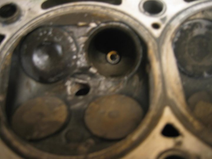 Pistonheads - The image presents a close-up view of a metal object, likely a part of an engine or machinery, characterized by a rusted surface. The object features an array of holes along its outer edge, possibly for mounting or part of a design feature. A hole devoid of rust is located in the center, surrounded by the undisturbed rust. This rust pattern gives the object an intricate and somewhat aged appearance. The background is indistinct, offering no additional context about the environment or the purpose of this object.