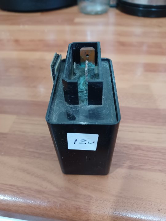 What is this black box? - Page 1 - In-Car Electronics - PistonHeads UK - The image displays a black plastic box labeled "12V 0.5A" with a single metal terminal visible on the inside of the box. It appears to be an electronic component, likely a battery or power supply unit. The box is set against a wooden table or countertop, and there's a faint outline of a person, possibly suggesting someone took the photo.