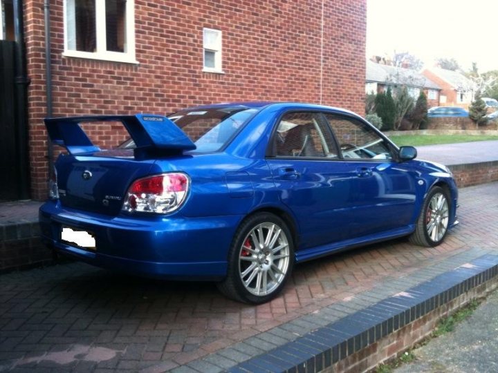 Everyones Wagons Jap Pistonheads - The image shows a blue, two-door coupe parked on a brick driveway. The car has a distinctive rear spoiler that is blue in color, matching the rest of the vehicle. The vehicle features alloy wheels on both the front and rear, adding to its sporty look. The license plate is visible at the front of the car, and there's a rear view that shows the side profile of the vehicle. The building in the background appears to be a residential house, suggesting a suburban setting.