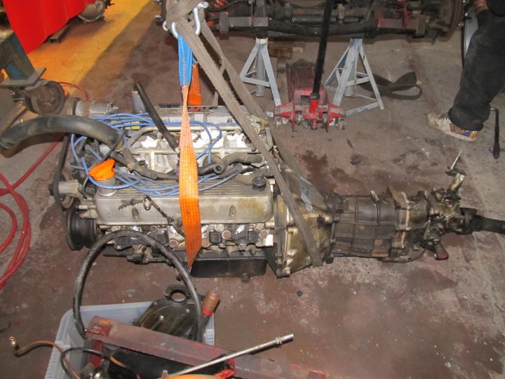 Pistonheads - The image showcases a busy repair scene with a silver engine removed from a vehicle and lying on its side on a concrete floor. This engine is part of a larger mechanical assembly, with cables and hoses attached to it, suggesting it's undergoing testing or maintenance. There are various tools scattered around the engine, indicating ongoing work. There's also a person standing by the engine, likely involved in this mechanical work. The surrounding area appears to be an industrial or garage setting, given the presence of other equipment and machinery in the background.