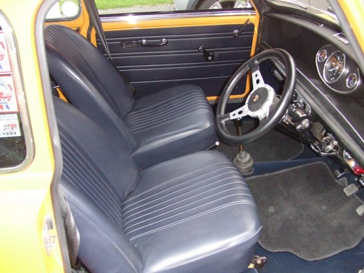 I've scratched a 25 year itch - My new '71 Mk3 Cooper S - Page 2 - Readers' Cars - PistonHeads - The image shows the interior of an old model car, specifically focusing on the driver's seat. The seat appears to be a vinyl material, likely a bench or pick-up truck seat, with visible stripes on the backrest. On the top, a small steering wheel is positioned with a gear shifter on the side. The front of the vehicle is partially visible, featuring a bright yellow color, which contrasts with the blue and black colors of the seat interior and the dash panel.