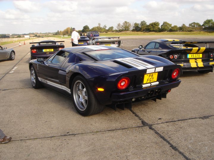 Supercars spotted, some rarities (vol 6) - Page 469 - General Gassing - PistonHeads - The image showcases a parking lot where several sports cars are displayed. The most prominent among them is a sleek, black Lamborghini roadster with distinctive orange brake lights. This particular Lamborghini is marked as "TT8". The roadster's position suggests it is on display, possibly indicating that it's being showcased, possibly in a show or exhibition. Of course, the setting also includes other vehicles, a few of which are also sports cars, though they are not as noticeable as the Lamborghini. The vehicles are parked on a concrete surface, with a grassy area and more cars visible in the background.