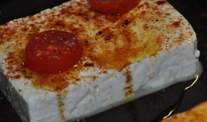 Competition Cooking Pistonheads Cheese - The image showcases a dish of farmers cheese with tomatoes, lightly dusted with herbs and spices. It's a close-up shot, focusing on the vivid colors and textures of the ingredients. The cheese appears to be in the form of a log or block, while the tomatoes provide a contrasting red. There is also a hint of smoky flavor from the seasonings sprinkled on top. The dish is appetizing and seems ready to be served or enjoyed.