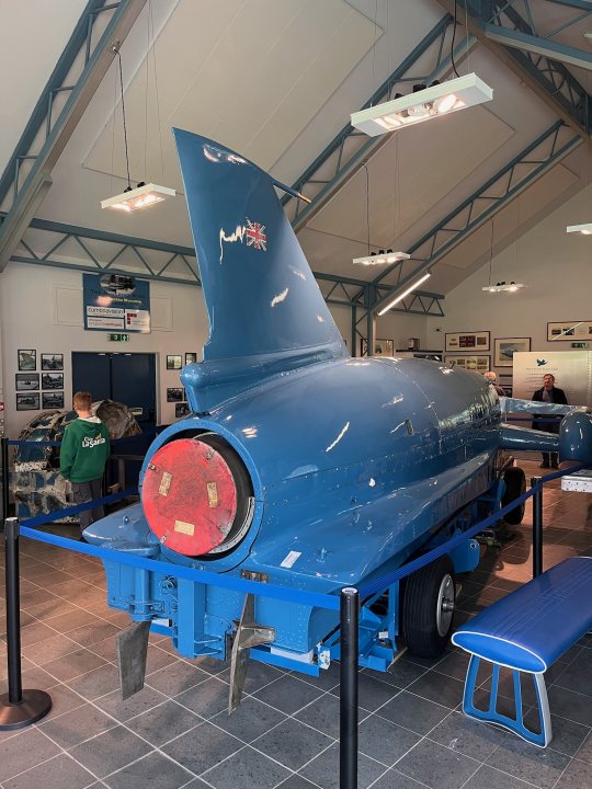 Pistonheads - The image showcases a blue jet engine displayed in an indoor setting. It's mounted on a metal stand, likely for protection or ease of viewing. A large hanger forms the backdrop, with the engine positioned towards the right side of the photo. There are no people present in this view. The scene exudes a sense of anticipation, as if waiting to be explored further.