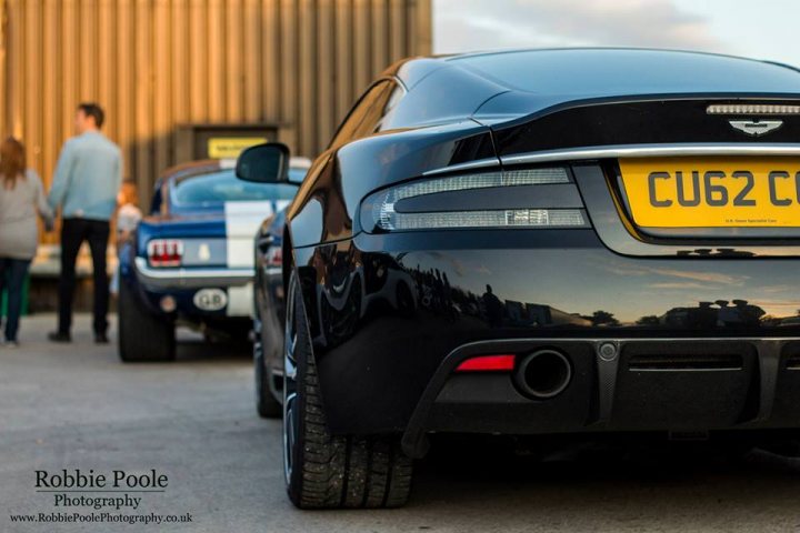 The GT Cafe - the ace cafe of the north - Aug meet - Page 1 - North West - PistonHeads - The image showcases a scene with a blue Audi R8 convertible parked prominently in a lot. The car takes up a large portion of the frame, with its black hood visible. There are two individuals standing behind the car, adding a sense of depth and scale to the image. In the background, there is another blue car, adding to the context of a parking lot. On the bottom left of the image, there is visible text that reads "Robbie Pole Photography." The overall atmosphere of the image suggests a casual, outdoor setting.