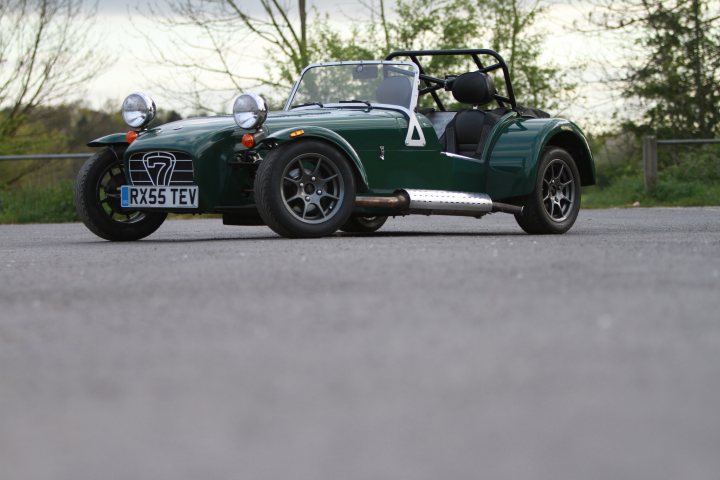 I've got one , after 7 months of searching....... - Page 1 - Caterham - PistonHeads - The image features an older, classic four-wheeled automobile with a unique design, similar to those used for driving on snow and ice. The car is painted in a shade of green or dark teal. It appears to be in good condition and is situated in a parking area outside with an unpaved surface. The wheels have large, spoked rims suitable for off-road use. The vehicle's license plate has the alphanumeric "RX5 TWV" displayed on it. There are no indications of use or recent travel. The background suggests an outdoor setting with trees and what appears to be foliage, suggesting the photo may have been taken during a time of the year where trees are still lush.