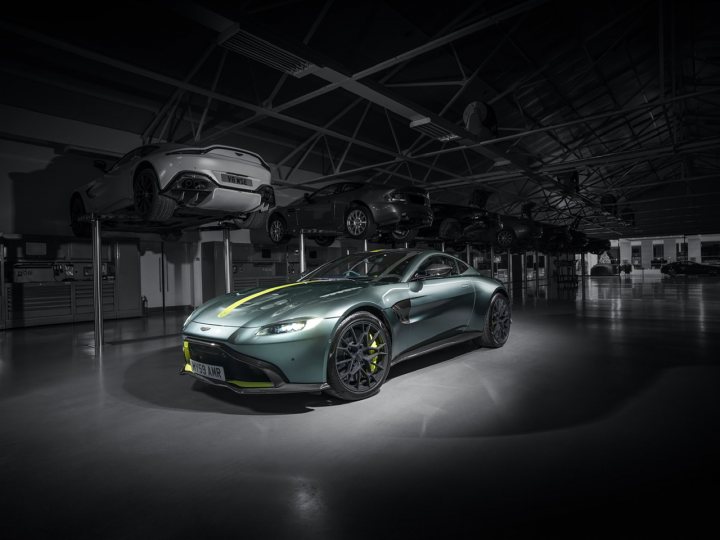 Vantage AMR 59 Edition Enjoy!! - Page 1 - Readers' Cars - PistonHeads - This image showcases a vibrant green Aston Martin sports car, which is the central focus of the scene. The car is positioned in an indoor setting, specifically within what appears to be a garage or showroom. It's parked in front of a wall that features the logos of several luxury car brands. The overall lighting and composition give the image a sophisticated and high-end feel.