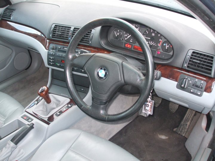 Pistonheads - This image shows the interior of a BMW car. The focus is on the driver's side, where a steering wheel with the BMW logo in the center is visible. The steering wheel is attached to a dashboard that displays a cluster of vehicle gauges, including a speedometer and a tachometer, with red, white, and black indicators. The steering wheel is positioned behind a gear shift lever, suggesting a manual transmission system. A key chain is hanging from the steering wheel, indicating a secure surface for personal belongings. The car's interior appears neat and well-maintained.