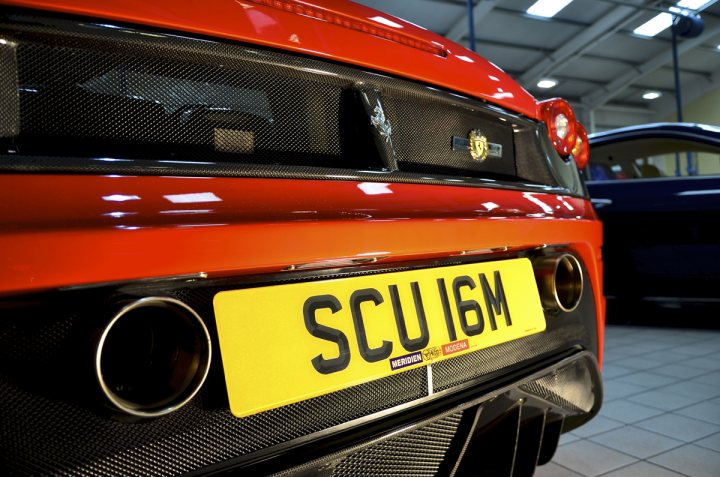 A red and yellow bus parked in a parking lot - Pistonheads - The image captures a close-up view of the back of a bright red car. The distinctive design of the car's exhaust pipe is visible, leading to a yellow license plate that displays the registration SCU 16M. The background reveals an indoor setting, likely a car show or garage, with other cars parked in the distance. The focus of the image is the vibrant red of the car and its detailing, particularly in the area of the exhaust pipe and license plate.