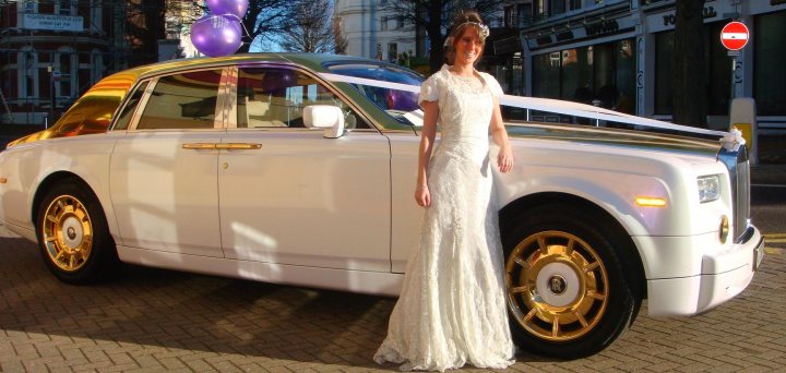 Perfect Wedding Pistonheads - In the heart of a cobblestone street, immaculately groomed and elegantly dressed in a traditional white bridal gown and a matching veil, a bride poses for the camera next to a vintage white Rolls Royce, its gold accents gleaming under the lighting. The car bears a diamond-shaped emblem on the hood, a testament to its nobility and refinement. The entire scene is bathed in soft, natural light, casting a romantic and celebratory ambiance.