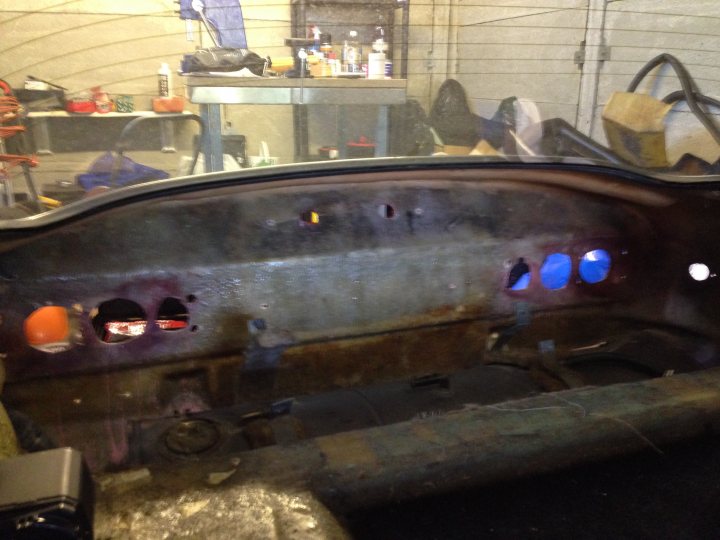 A close up of a car on a city street - Pistonheads - The image shows an open car hood revealing its rusted interior. Inside the hood, there are various mechanical components, including a red and white item that appears to be the engine. The vehicle appears to be a vintage car, as indicated by the aged doors and the rough condition of the hood. The car is situated in a garage, which has objects and equipment scattered around, suggesting a workspace rather than a showroom. There is no visible brand or make of the car in this particular shot.